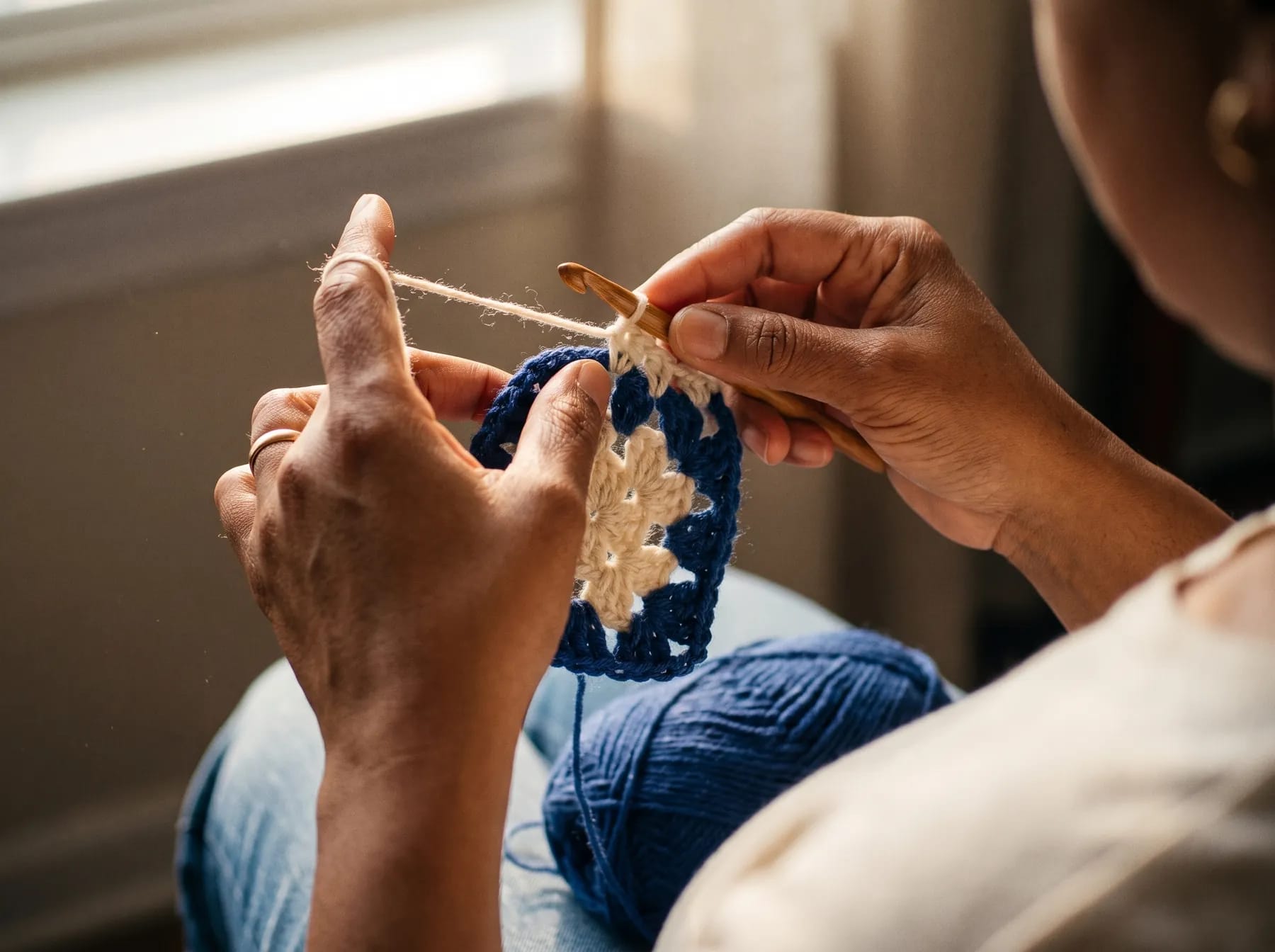 Gros plan sur des mains en train de crocheter un granny square avec un crochet en bois