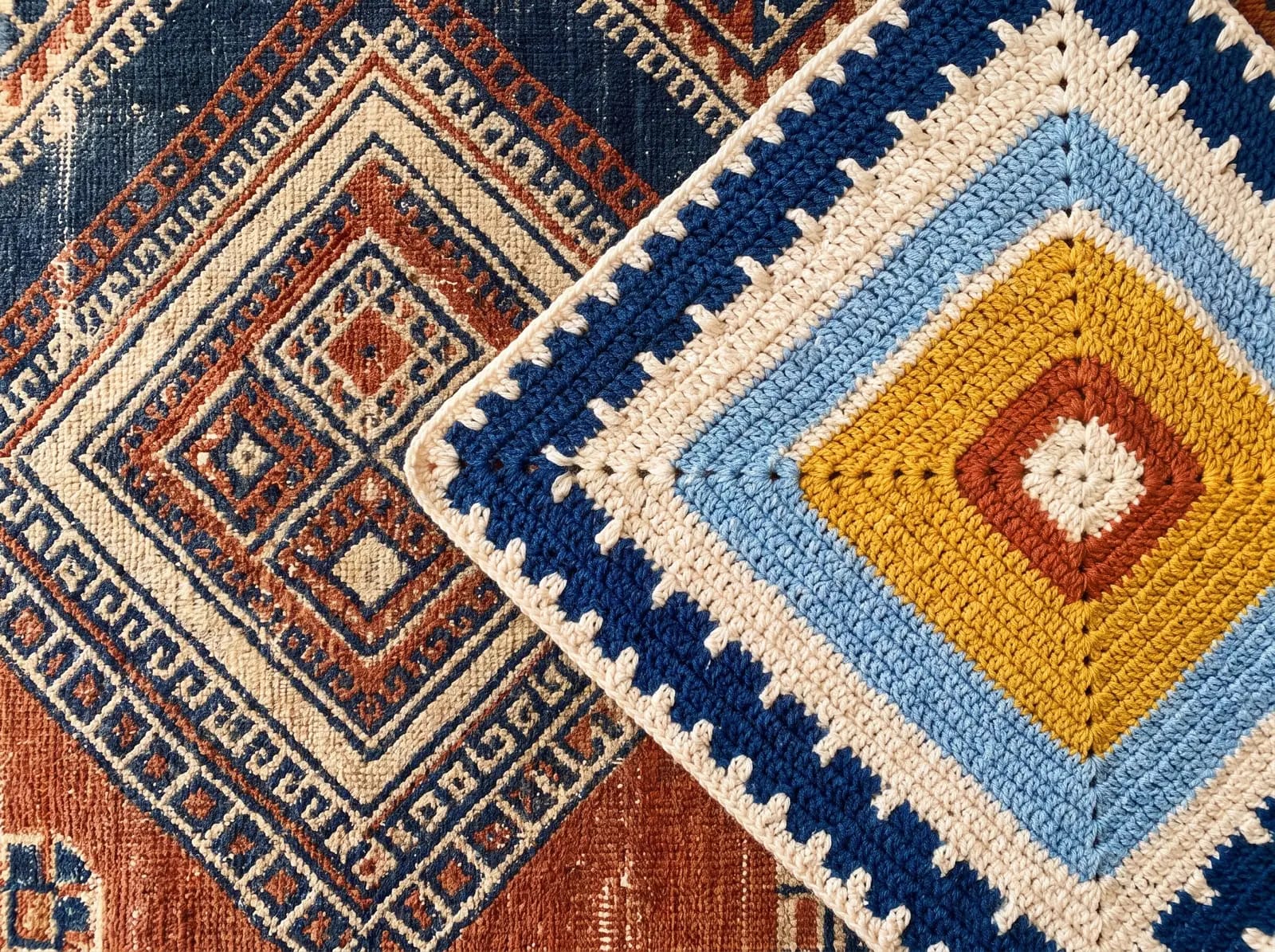 Le coin d'un tapis amazigh ancien posé à côté d'un granny square au crochet : la même grille de carrés concentriques